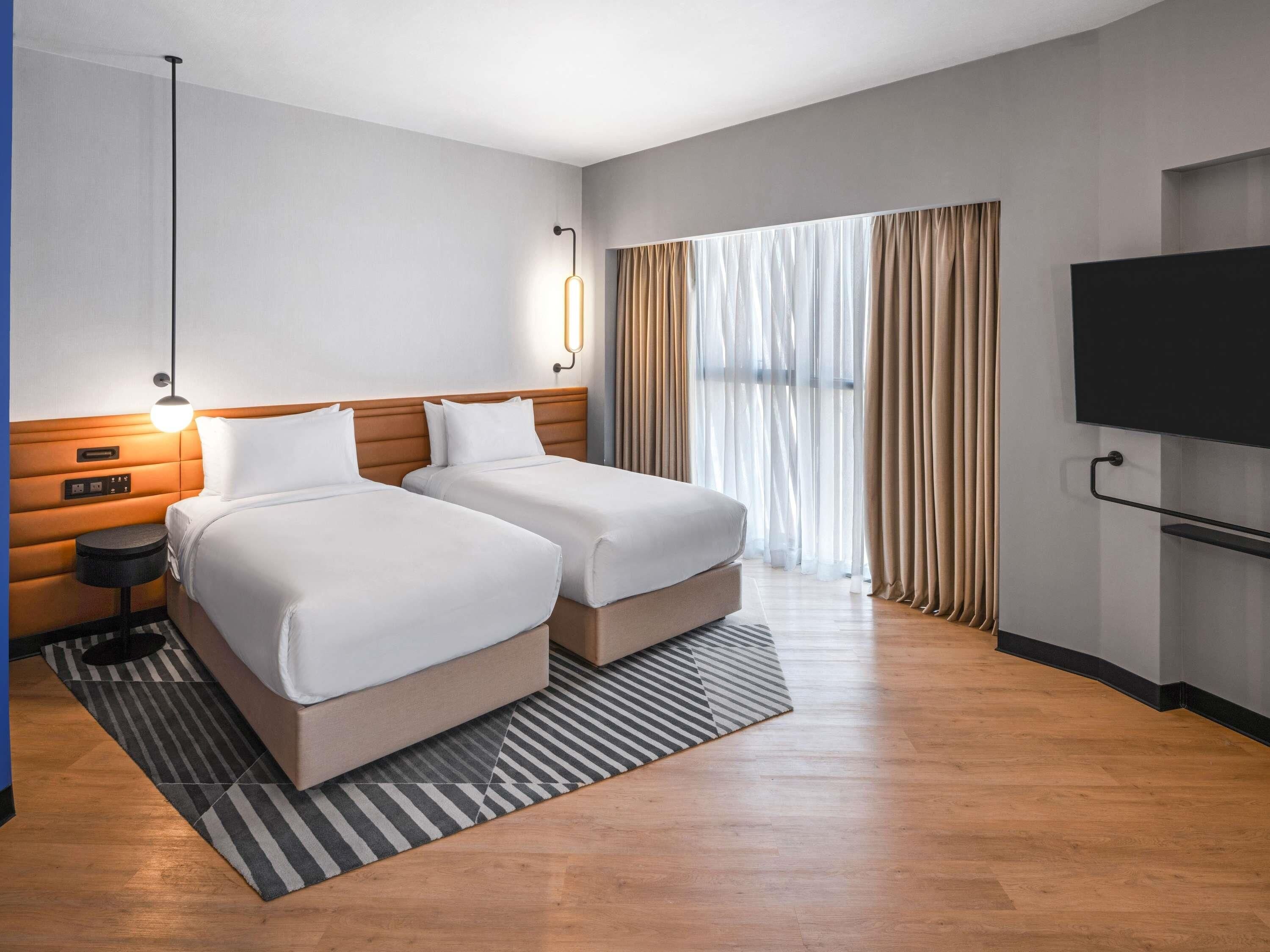 Une chambre d’hôtel avec deux lits, une télévision, une fenêtre avec des rideaux et un tapis à rayures.