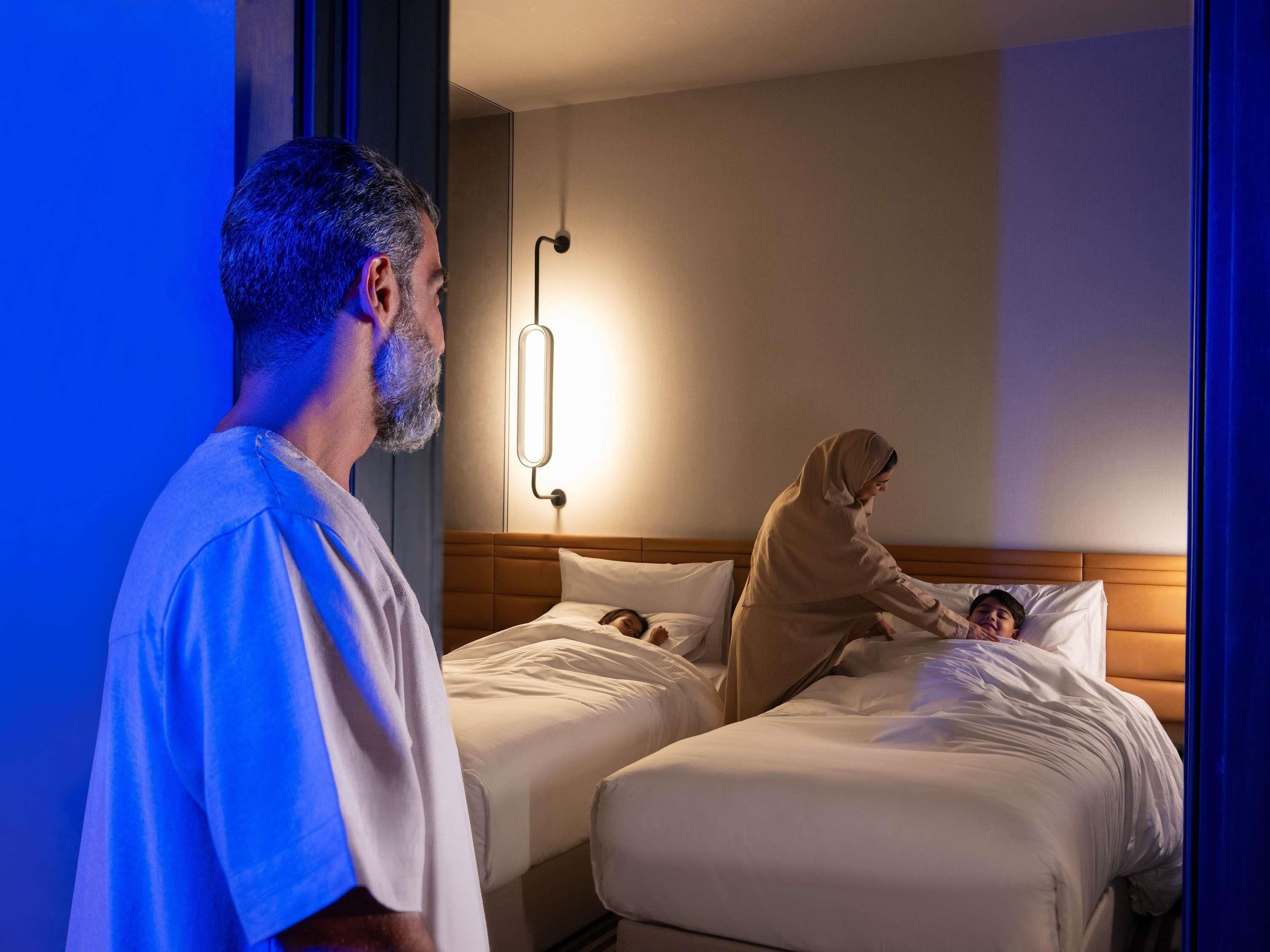 A hotel room with two beds, a nightstand, and a wall-mounted light fixture.