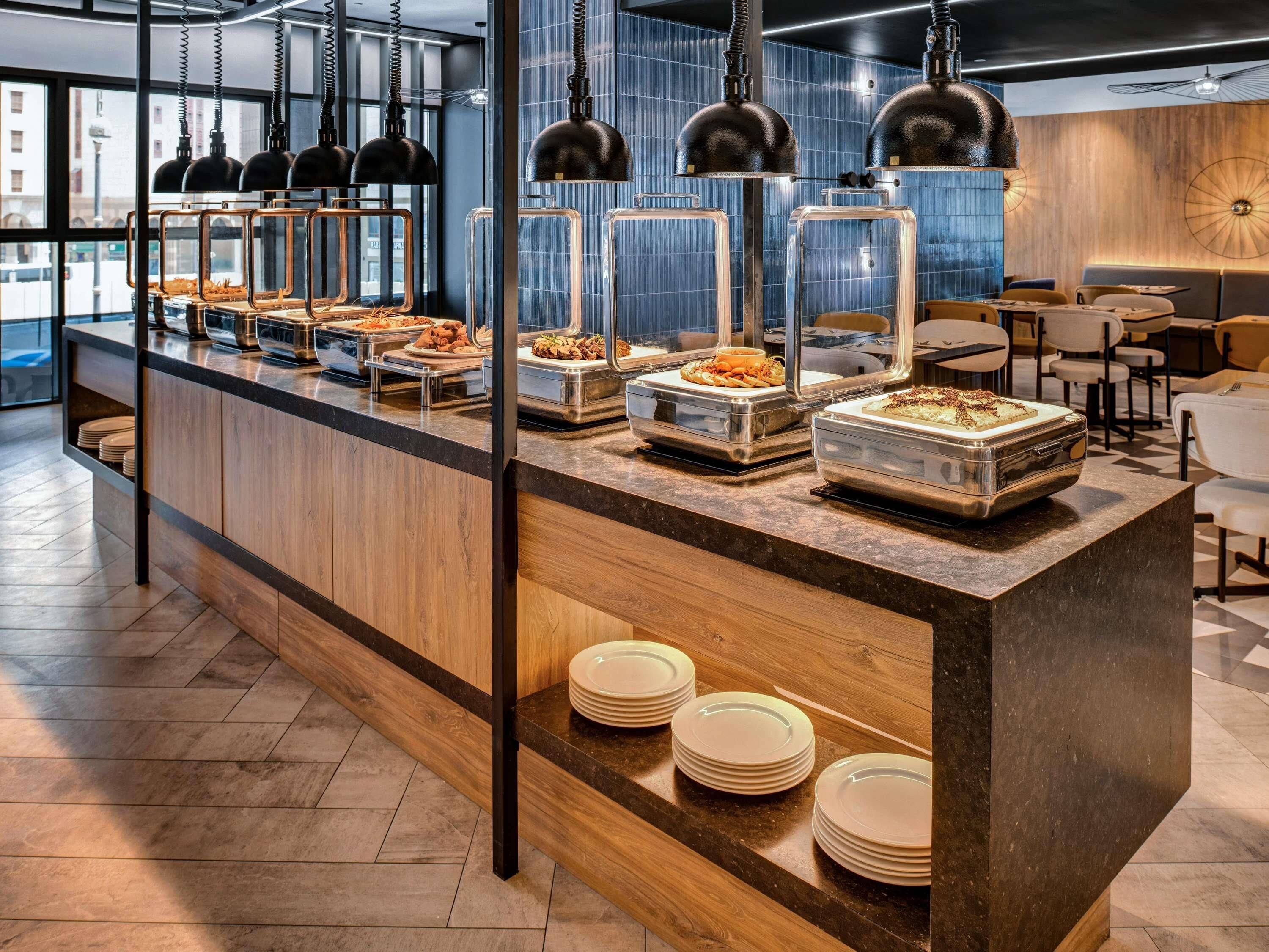 A buffet area with various food items, a counter with plates, and a seating area with tables and chairs.