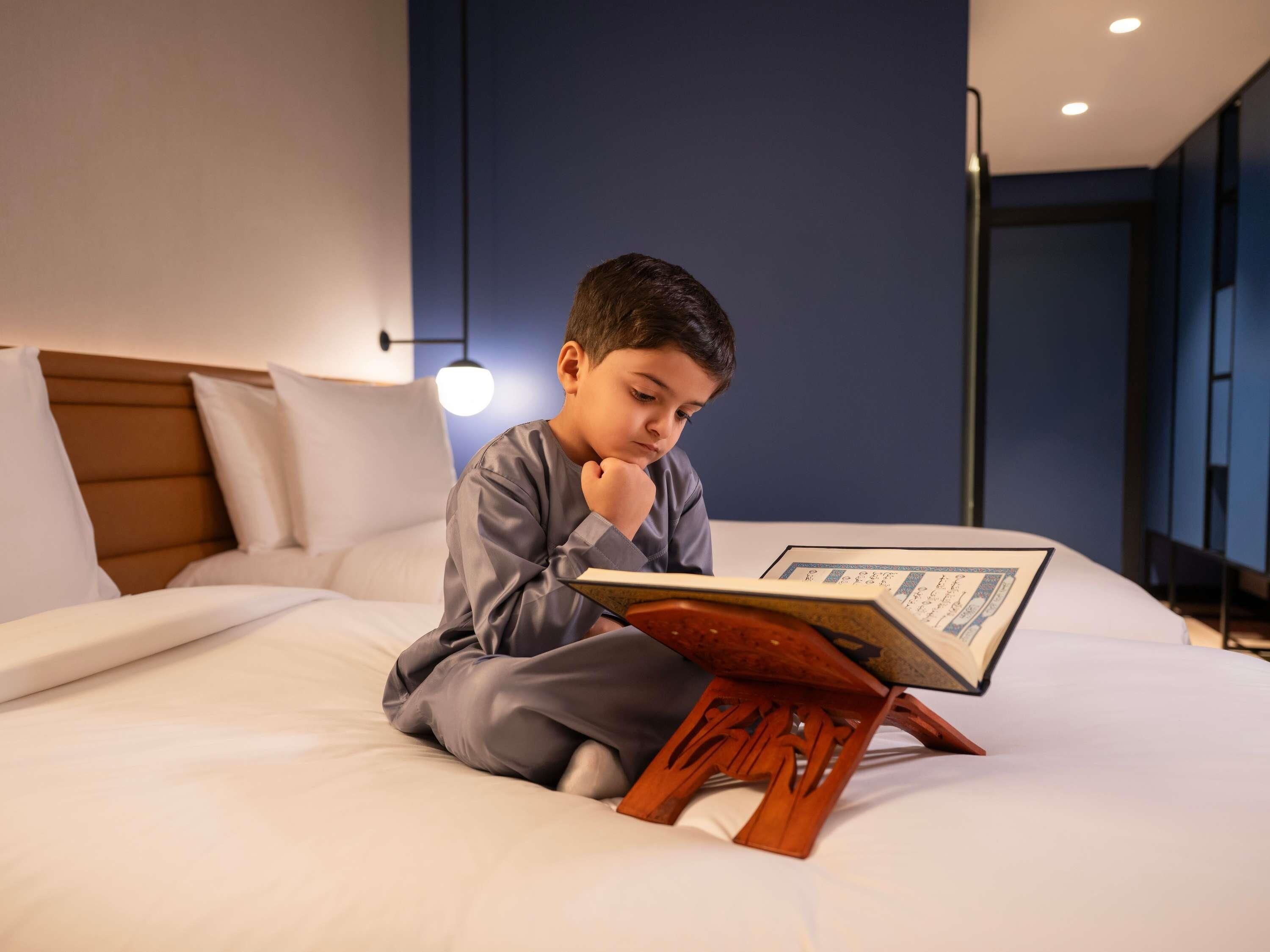 Una persona sentada en una cama con un libro, en una habitación de diseño moderno y con una lámpara de techo visible.