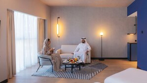 A modern hotel room with a sofa, a coffee table with breakfast items, a standing lamp, and a large window with curtains. - Novotel Madinah (Madinah)