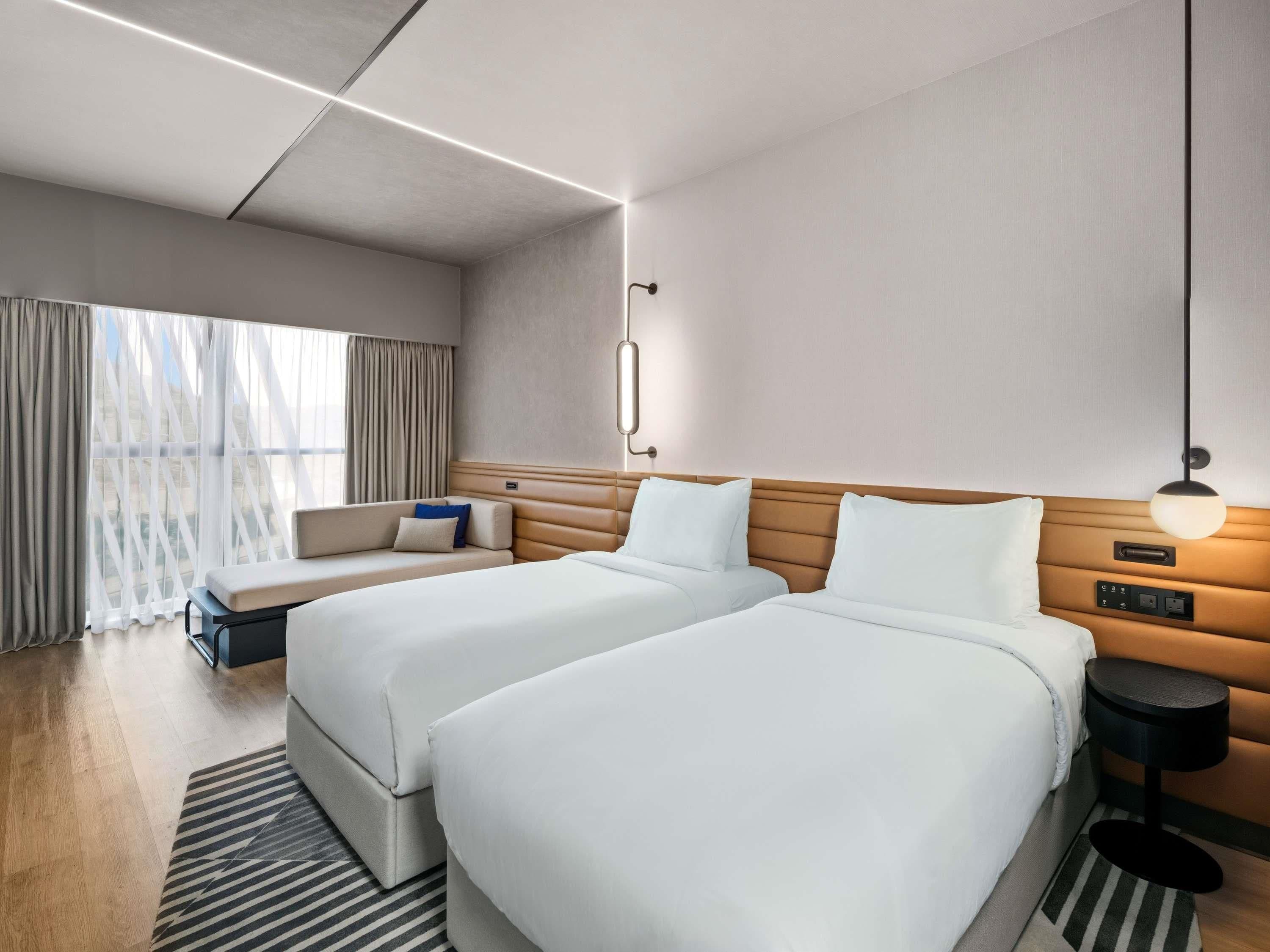 Une chambre d’hôtel avec deux lits, un canapé, une table de chevet et une lampe.