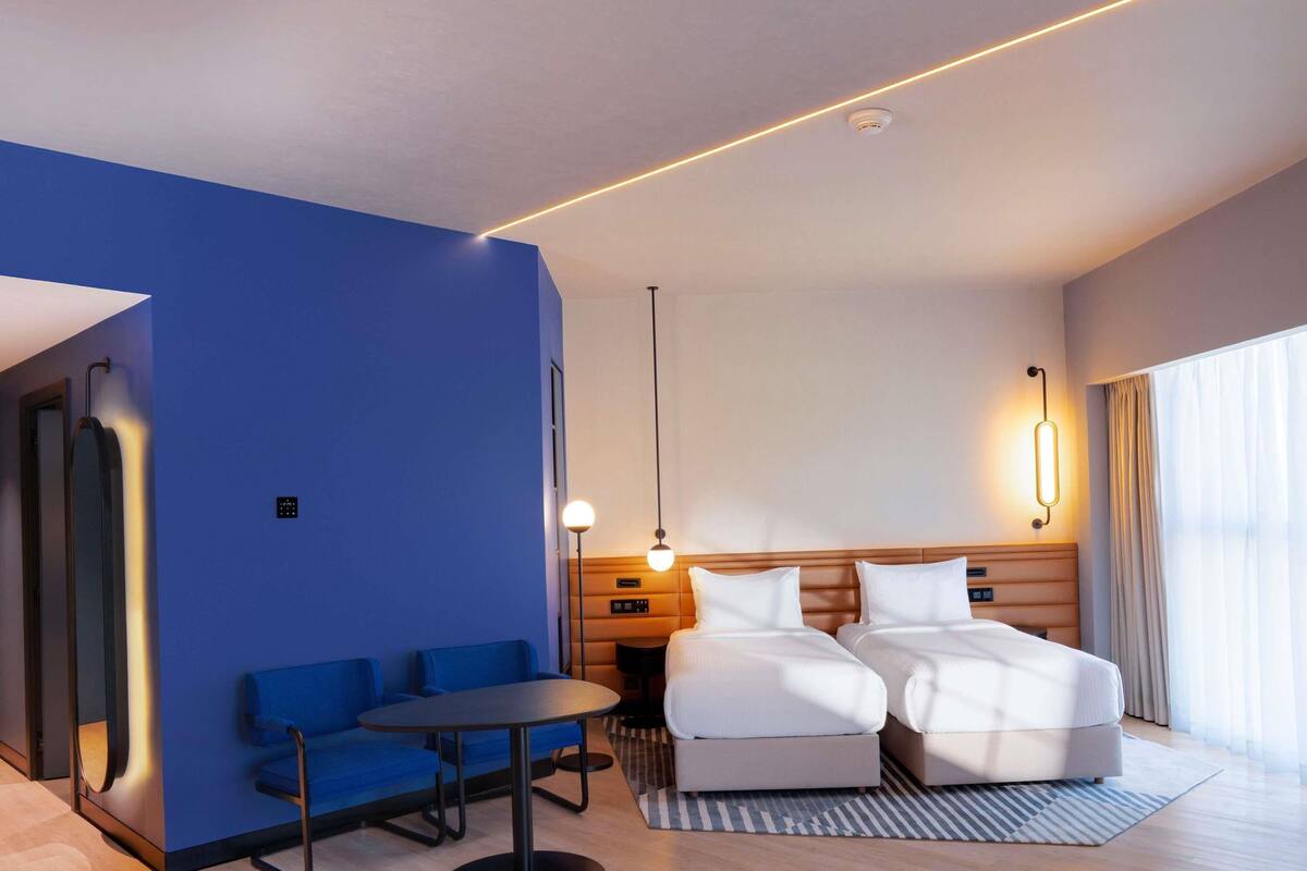 Una habitación de hotel moderna con una pared de acento azul, una cama con ropa blanca, una pequeña mesa redonda y un sofá azul.