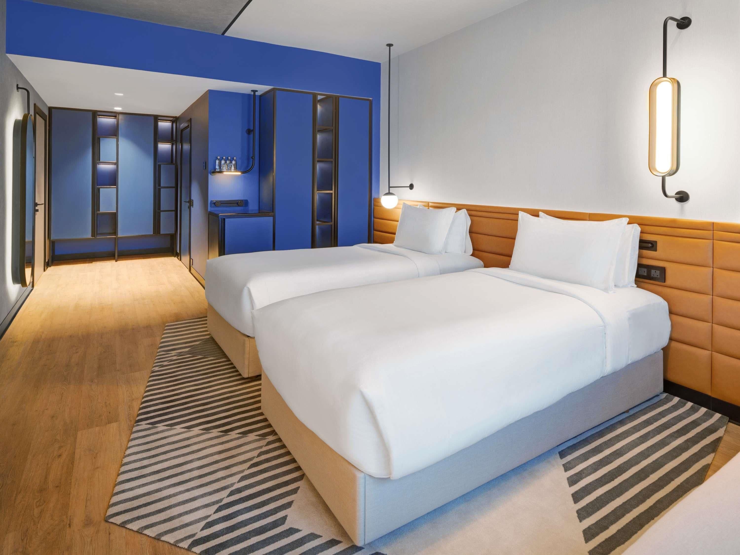 A hotel room with two beds, a blue accent wall, a wooden floor, and a striped rug.