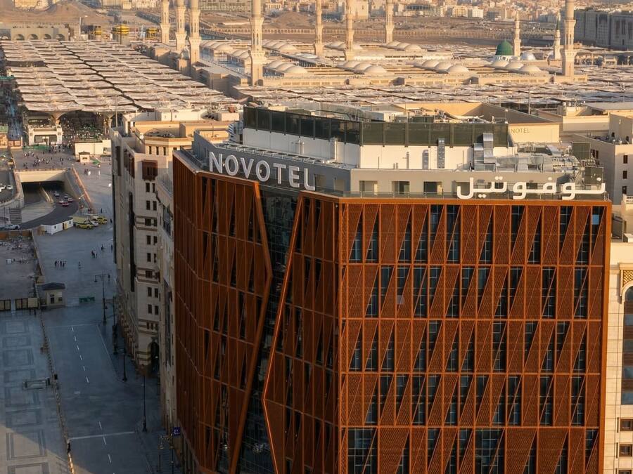 Un hôtel moderne à la façade géométrique originale, situé dans une ville où de grandes mosquées se dressent en arrière-plan.