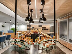 A modern interior with a central glass display of assorted appetizers, overhead lighting, and a wooden ceiling. - Novotel Madinah (Madinah)