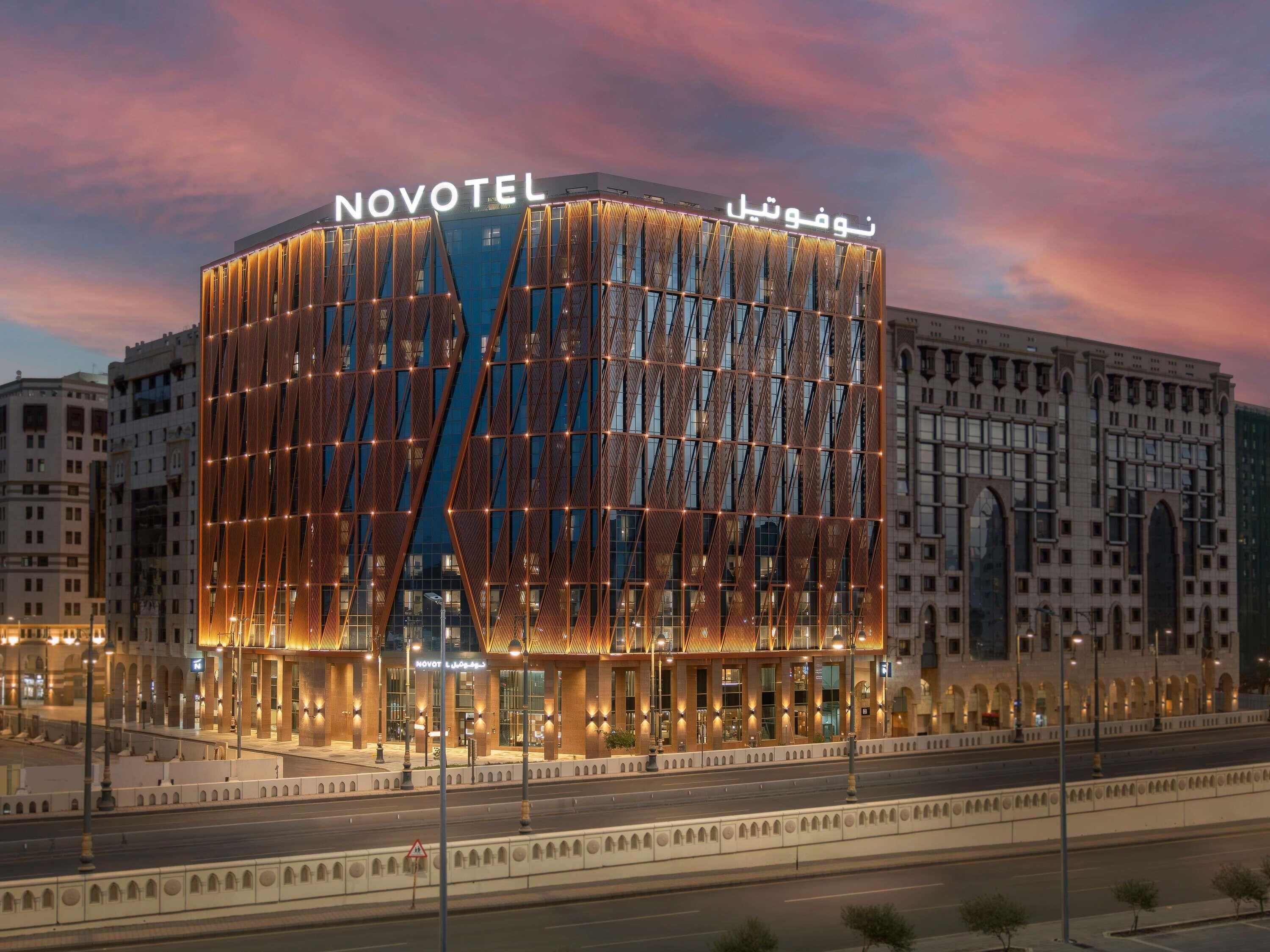 Un hotel moderno con un llamativo letrero 'NOVOTEL', que presenta una fachada geométrica única e iluminación cálida.