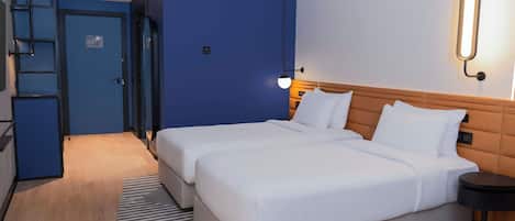 A hotel room with a double bed, a bedside table, a lamp, a blue wall, and a door.