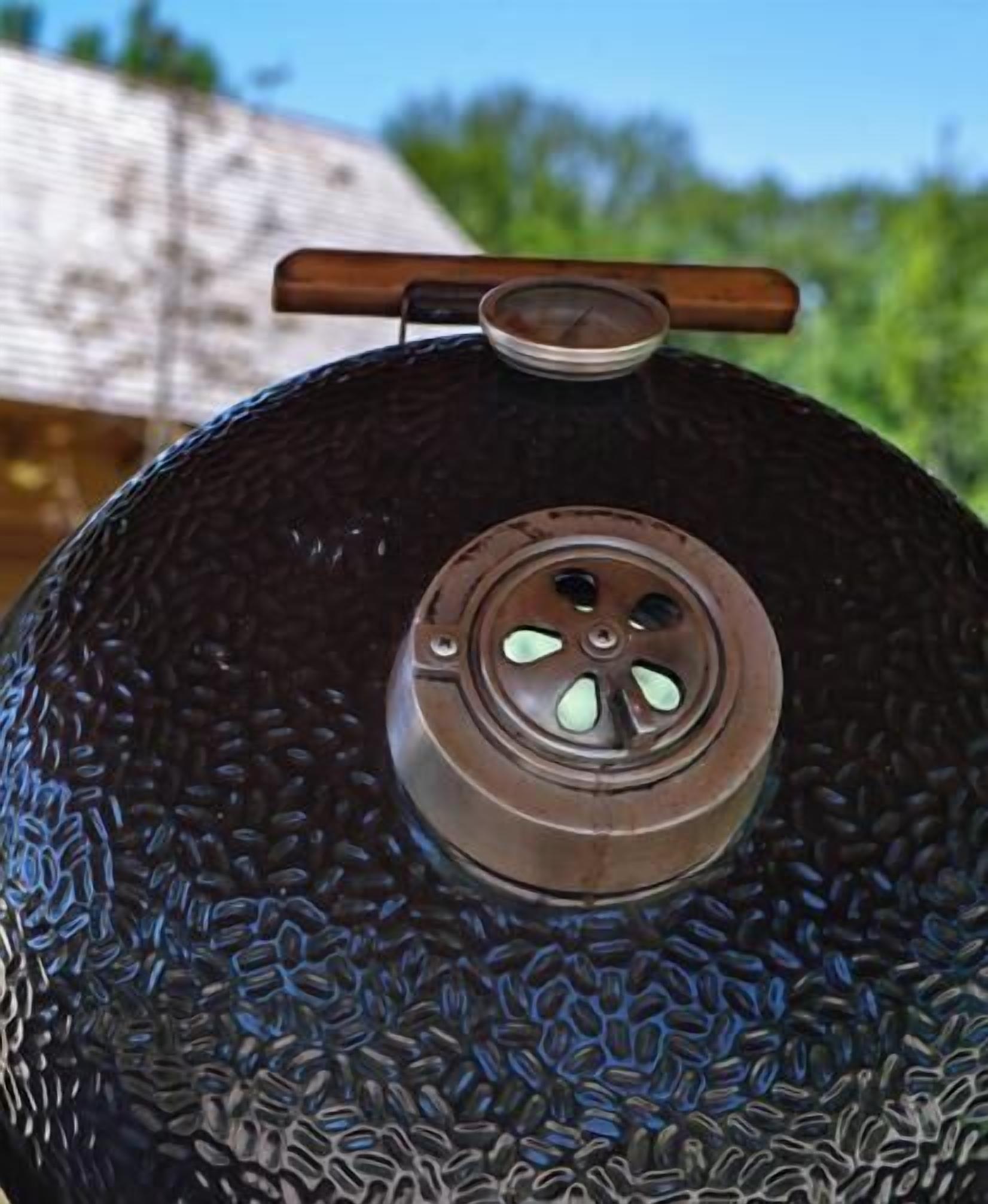 Ein großer, runder, dunkel gefärbter Grill mit Metallgriff und einem runden Lüftungsöffnungsloch obenauf.