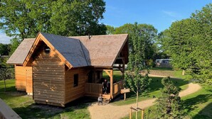A wooden cabin with a porch, surrounded by a grassy area and trees. - Unique overnight stay for true 'lovebirds' in our treehouse! (Uden)