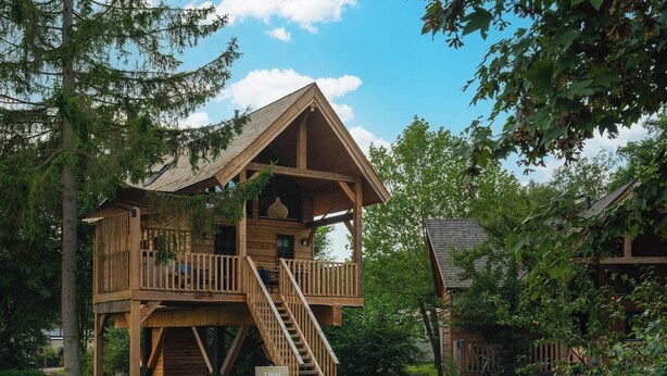 Une cabane en bois dotée d’un balcon et d’un escalier, entourée d’arbres.