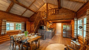 Ein Blockhaus-Interieur mit Essbereich, Küche und einer Treppe, die zu einer oberen Etage führt.
