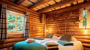Ein Schlafzimmer in einer Blockhütte mit einem Bett, Kissen und einem Fenster mit Vorhängen.