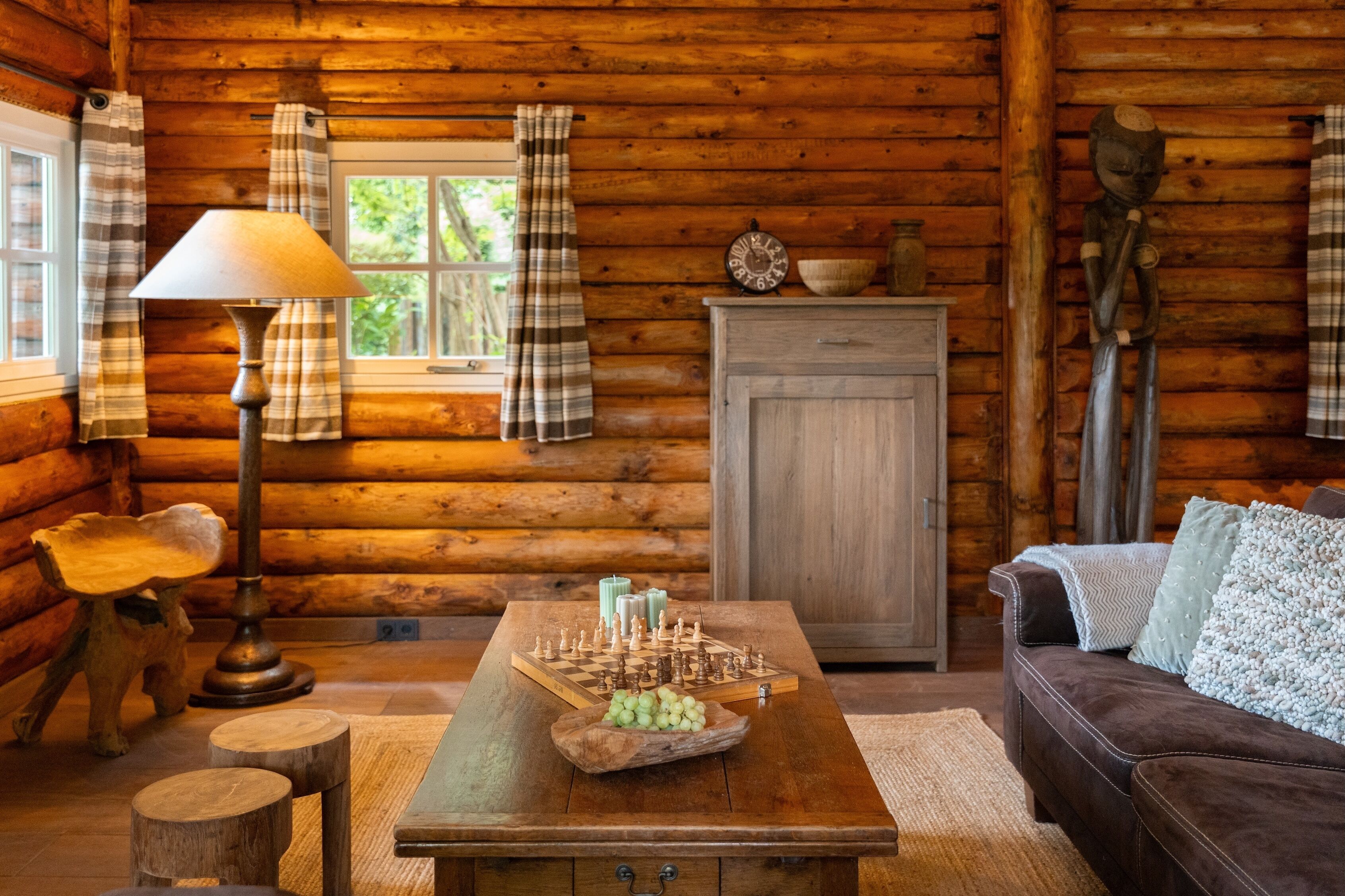 L’intérieur d’un chalet confortable, avec des murs en rondins de bois, une table en bois, une lampe, un jeu d’échecs et un canapé.