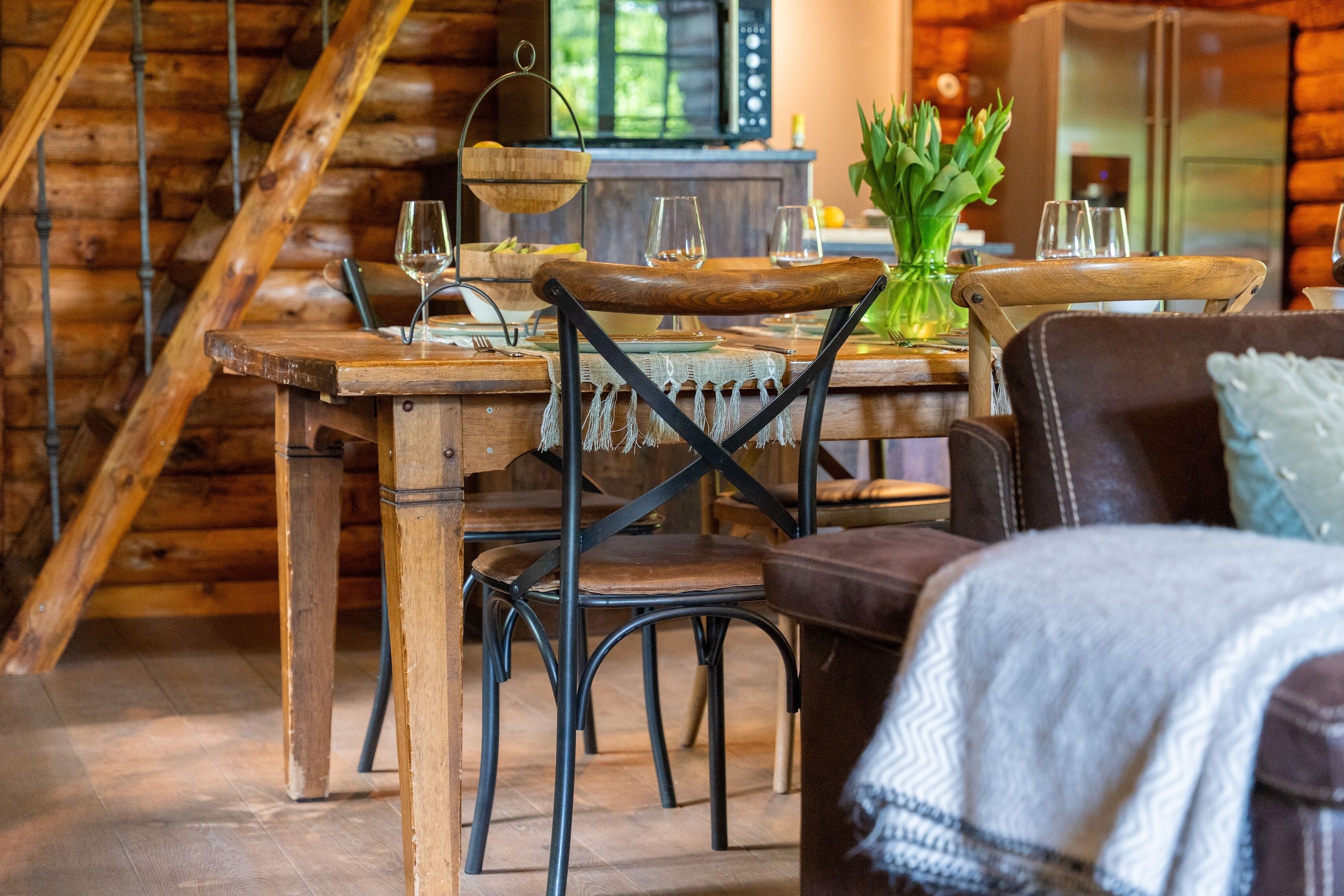 A rustic wooden dining area with a wooden table and chairs, a hanging light fixture, and a vase with green plants.