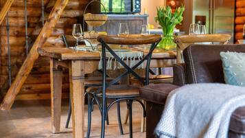 A rustic wooden dining area with a wooden table and chairs, a hanging light fixture, and a vase with green plants.