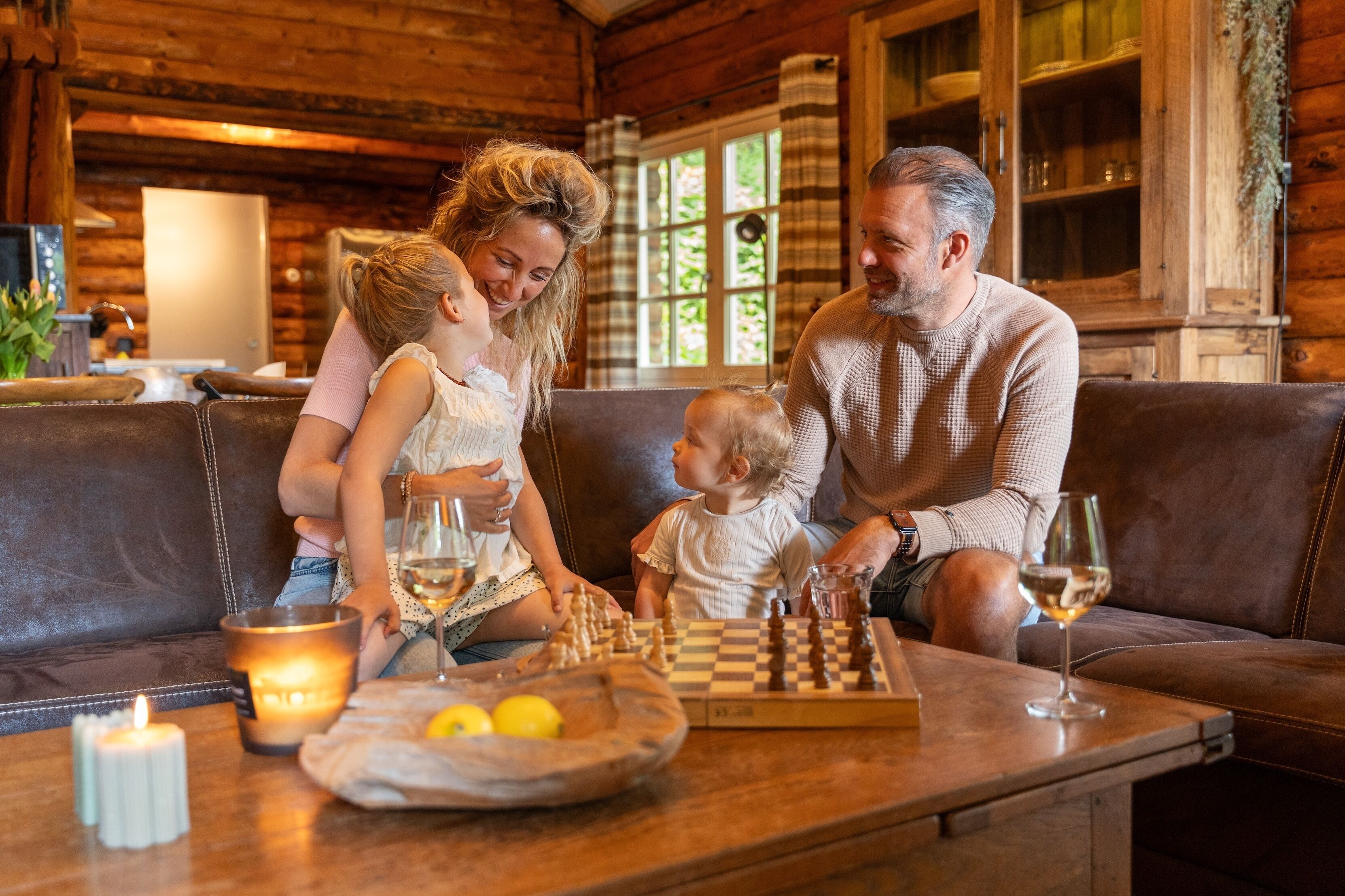 Een gezin speelt schaak in een gezellig chalet met houten inrichting, een tafel met een schaakbord en kaarsen op tafel.