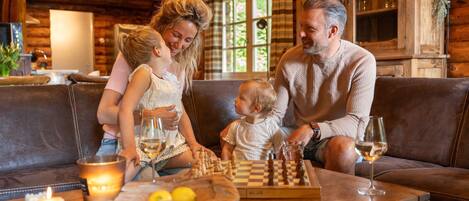 A family playing chess in a cozy cabin with a wooden interior, a table with a chessboard, and candles on the table.