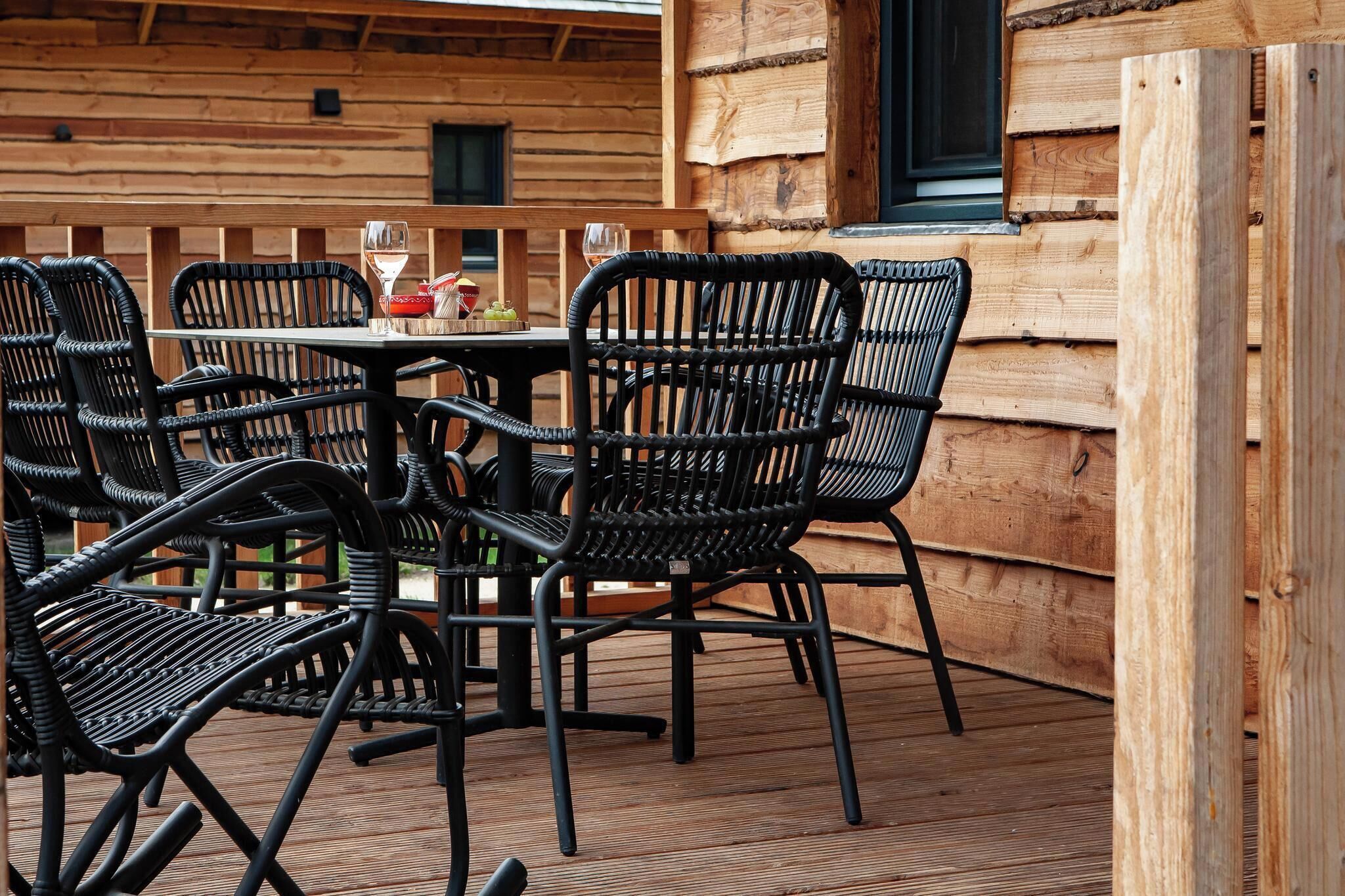 Een houten terras met een tafel, stoelen, een raam en een houten wand.
