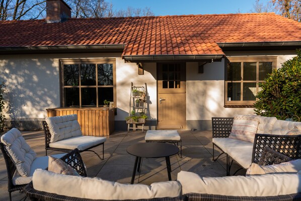 An outdoor patio with wicker furniture, a wooden bench, and a small table. - Ultimate luxury in this villa for 12 people, with sauna, jacuzzi, and direct access to the forest! (Uden)