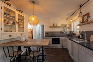 A modern kitchen with a wooden table, bar stools, a hanging light fixture, and stainless steel appliances. - Ultimate luxury in this villa for 12 people, with sauna, jacuzzi, and direct access to the forest! (Uden)