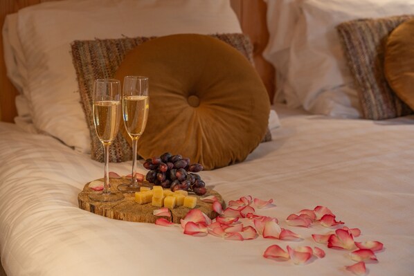 A bed with a wooden serving board holding cheese, grapes, and two glasses of champagne.