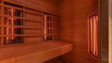 Een sauna met houten wanden en banken, met metalen gaasramen en een bank op de voorgrond.
