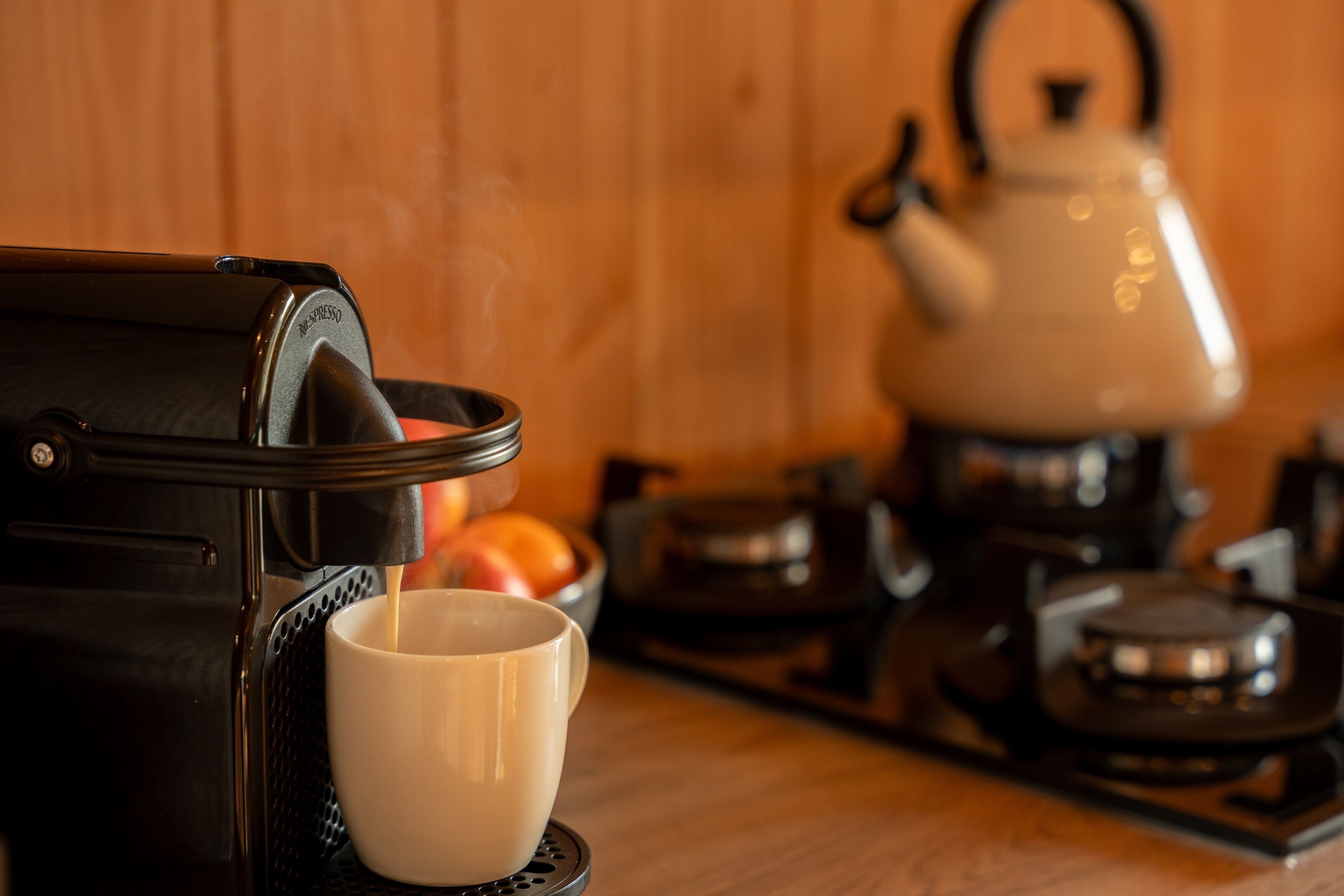 A coffee machine dispensing coffee into a cup, with a kettle and pots in the background.