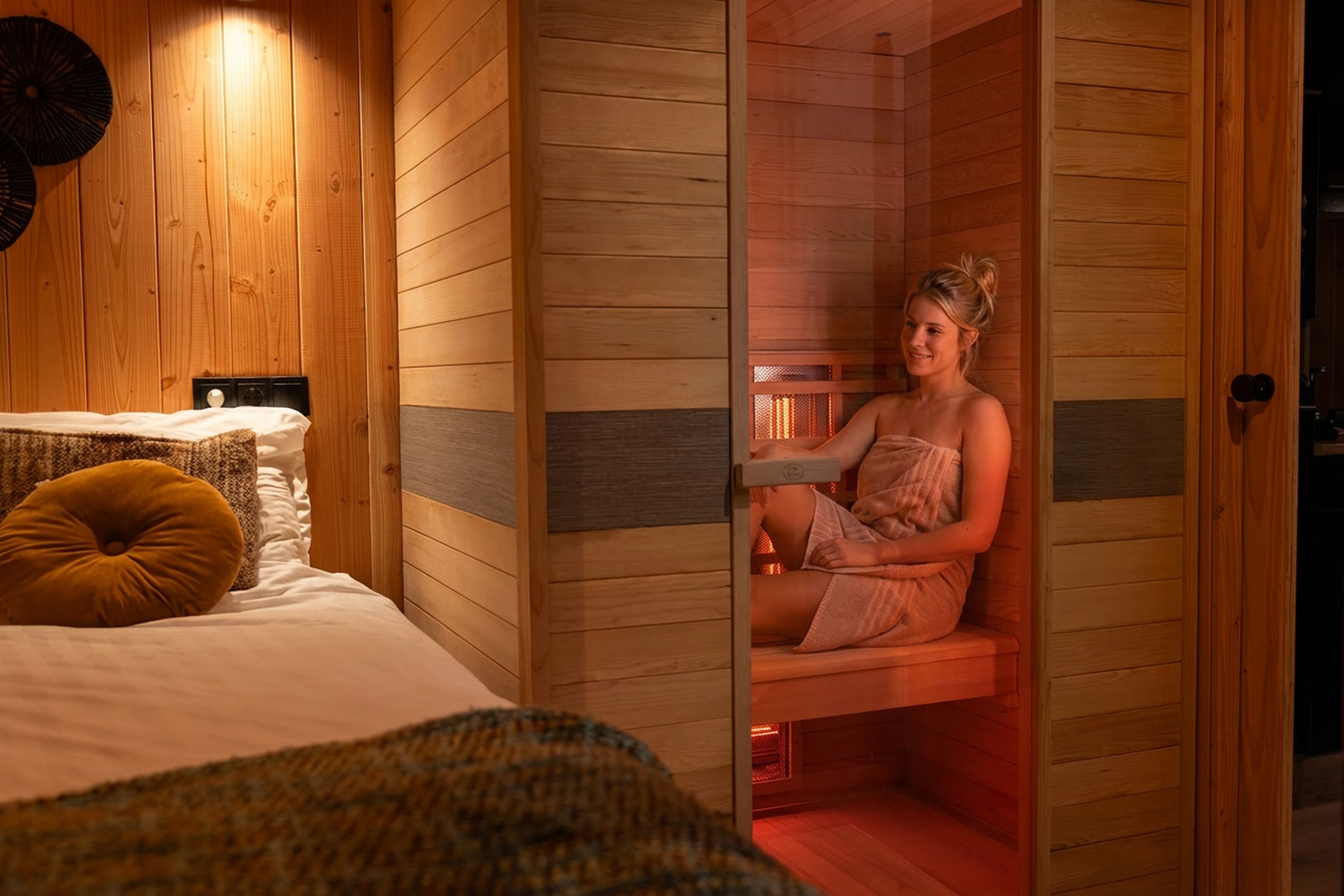 A wooden cabin with a sauna, a bed with a mustard-colored pillow, and a small table.