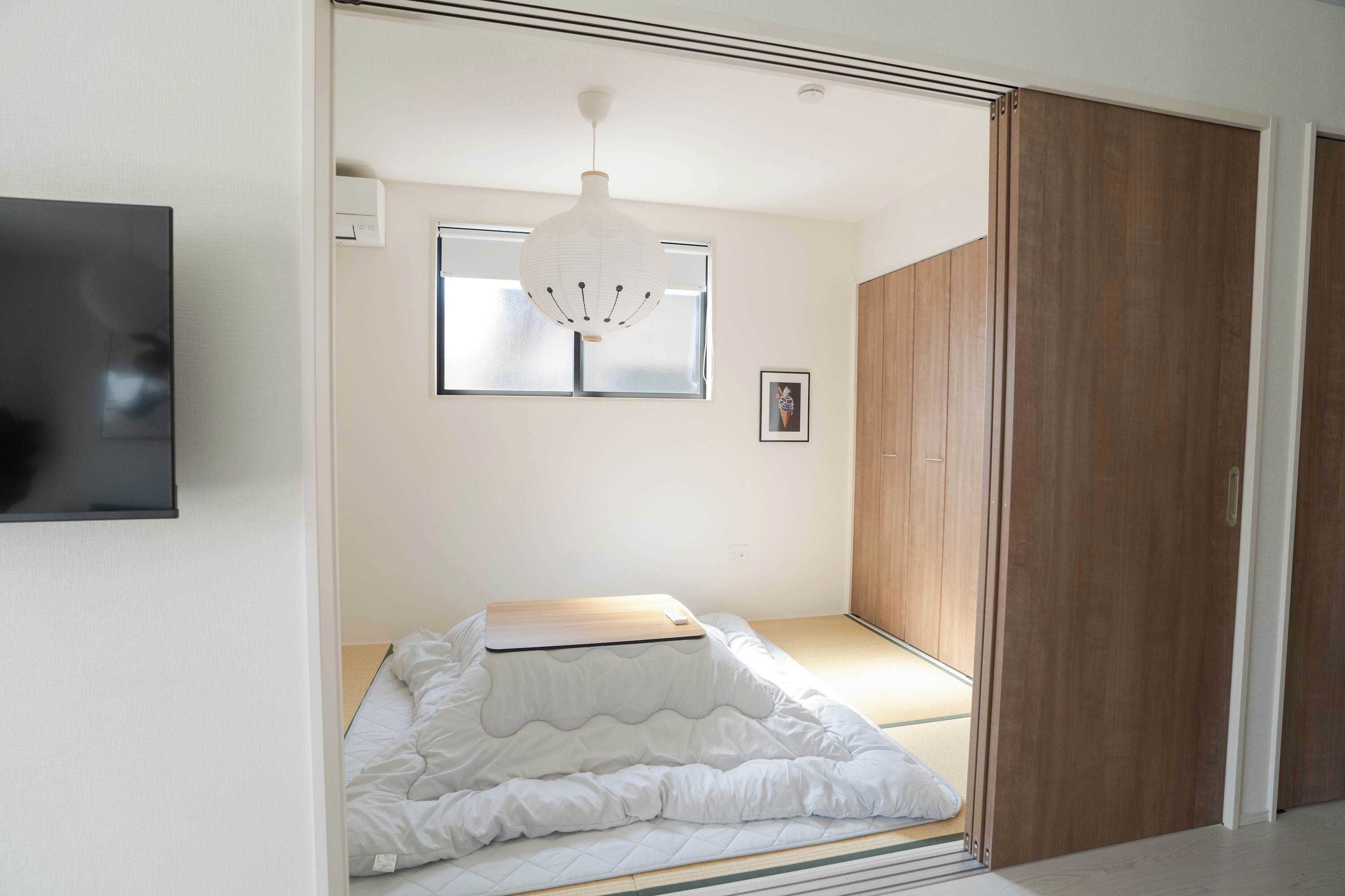 A bedroom with a bed, a wooden wardrobe, a window, and a hanging light fixture.