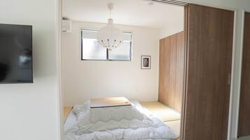 A bedroom with a bed, a wooden wardrobe, a window, and a hanging light fixture.