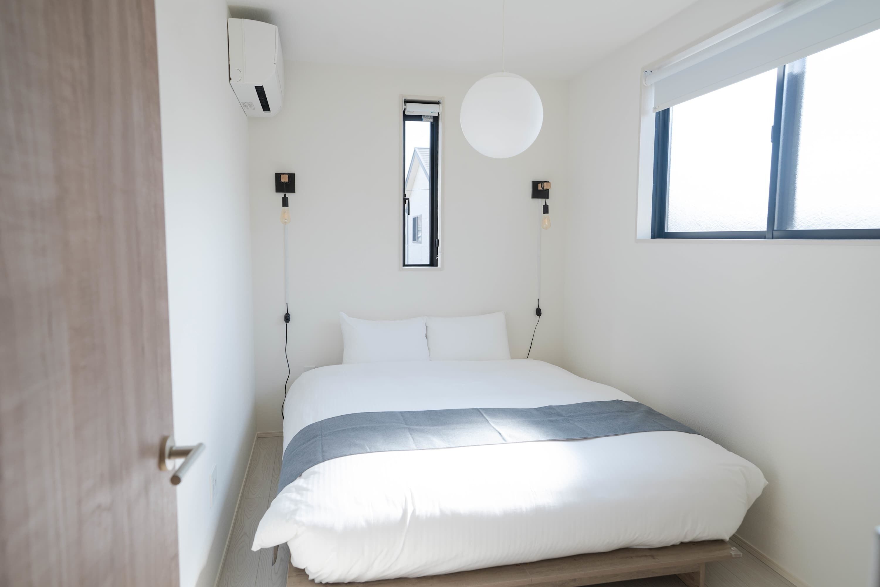 Ein Schlafzimmer mit Bett, Fenster, Wandklimaanlage und einer Leuchte.
