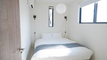 Ein Schlafzimmer mit Bett, Fenster, Wandklimaanlage und einer Leuchte.