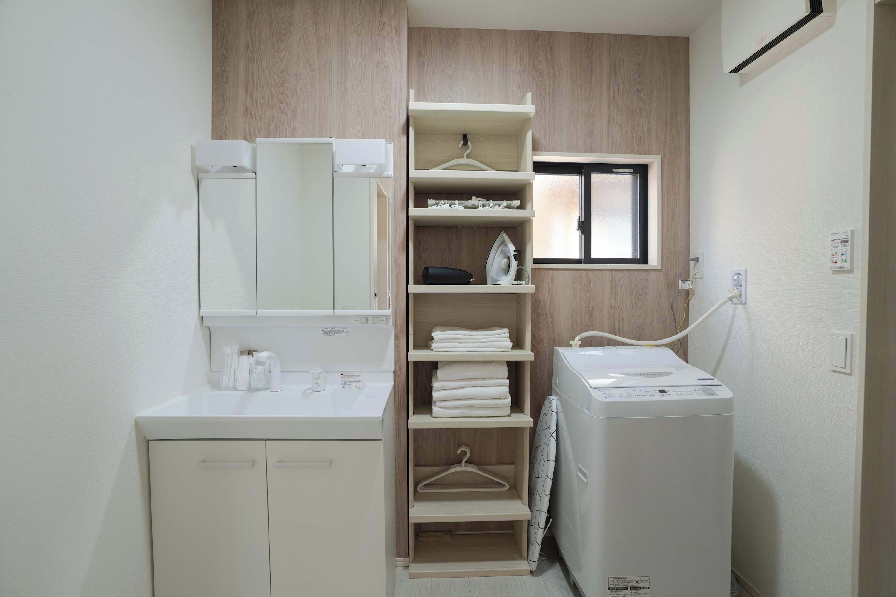 A compact bathroom with a built-in washing machine, a mirror, and a small window.