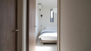 A bedroom with a bed, a bedside table, a wall-mounted air conditioner, and a window.