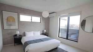 A modern bedroom with a large bed, bedside tables, a gray rug, a window, and an air conditioning unit.
