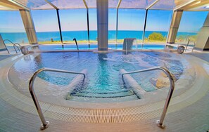 An indoor swimming pool with a view of the ocean, metal railings, and a tiled floor. - Casamaïa Apartments Affiliated by Meliá (Benalmádena)