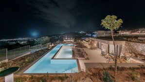 A nighttime view of a pool area with a rectangular pool, lounge chairs, and a stone wall. - Domaine Collection Sun Villa (Hersonissos)