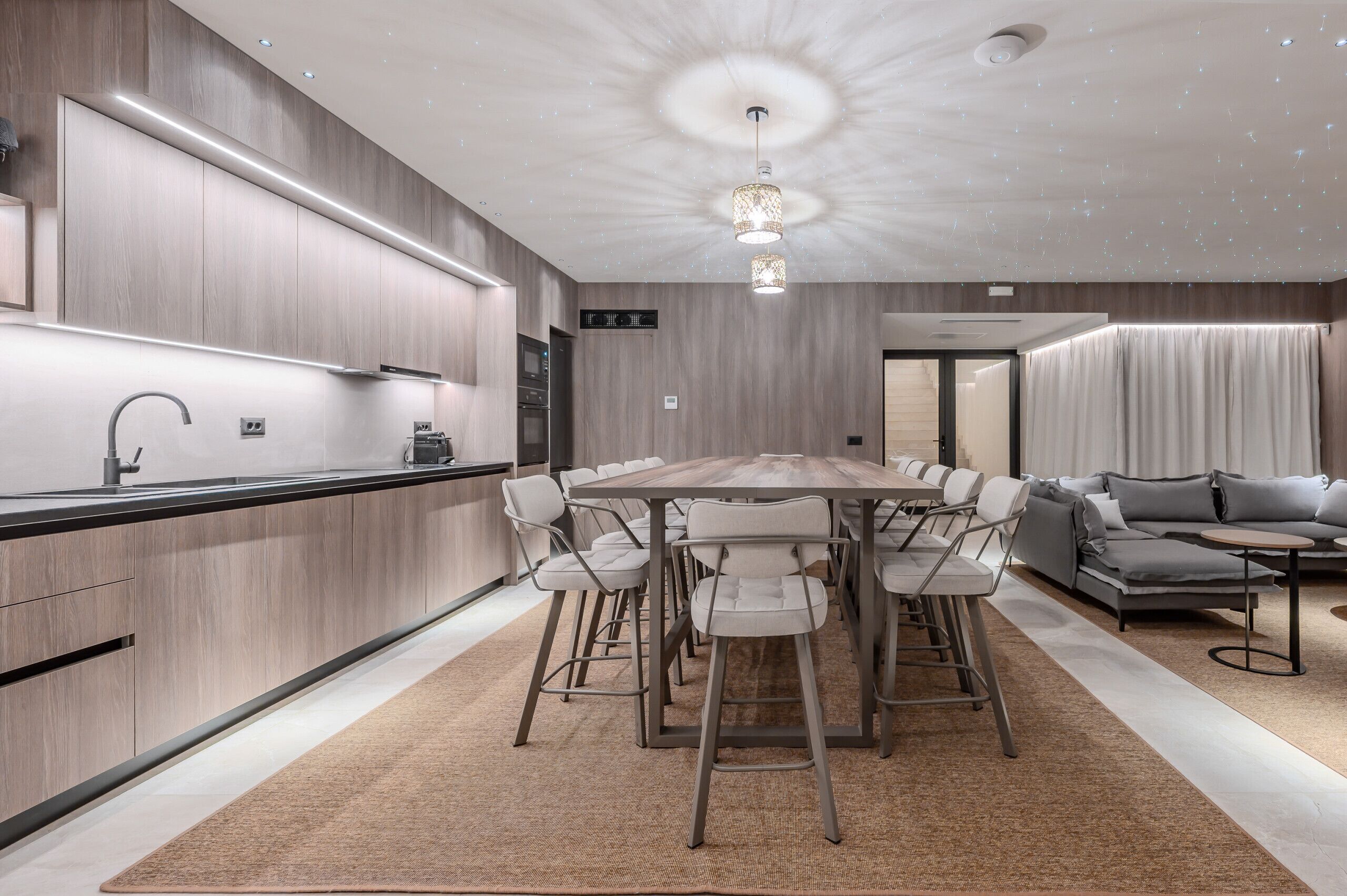 A modern kitchen with a central island, a dining area with chairs, and a sofa in a living area.