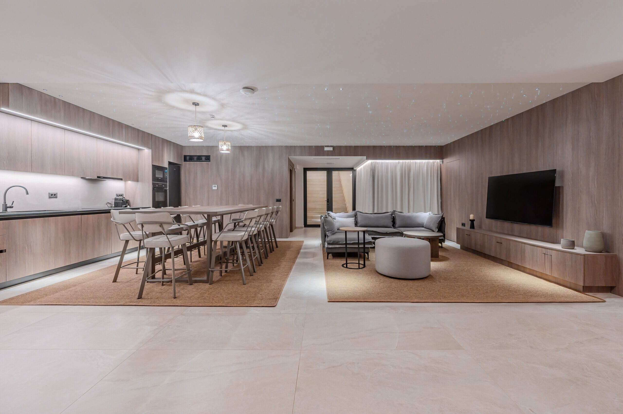 A modern kitchen with a dining area, a living room with a sofa and TV, and a staircase leading to another level.