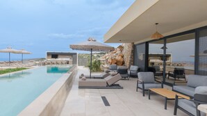 A poolside area with lounge chairs, a stone wall, and a view of the sea. - Domaine Collection Earth Villa (Hersonissos)