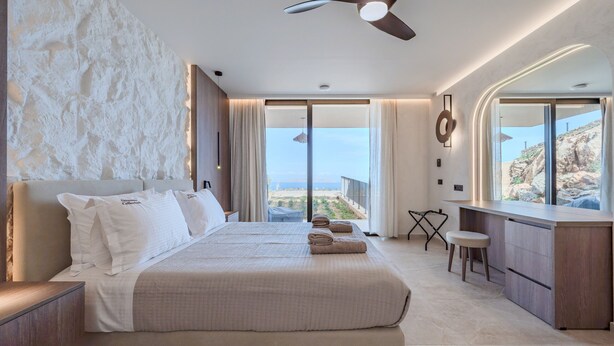 A modern hotel room with a large bed, a desk, and a view of the ocean. - Domaine Collection Earth Villa (Hersonissos)