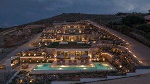 A multi-story hotel with a pool, outdoor seating, and a mountainous backdrop. - Domaine Collection Earth Villa (Hersonissos)