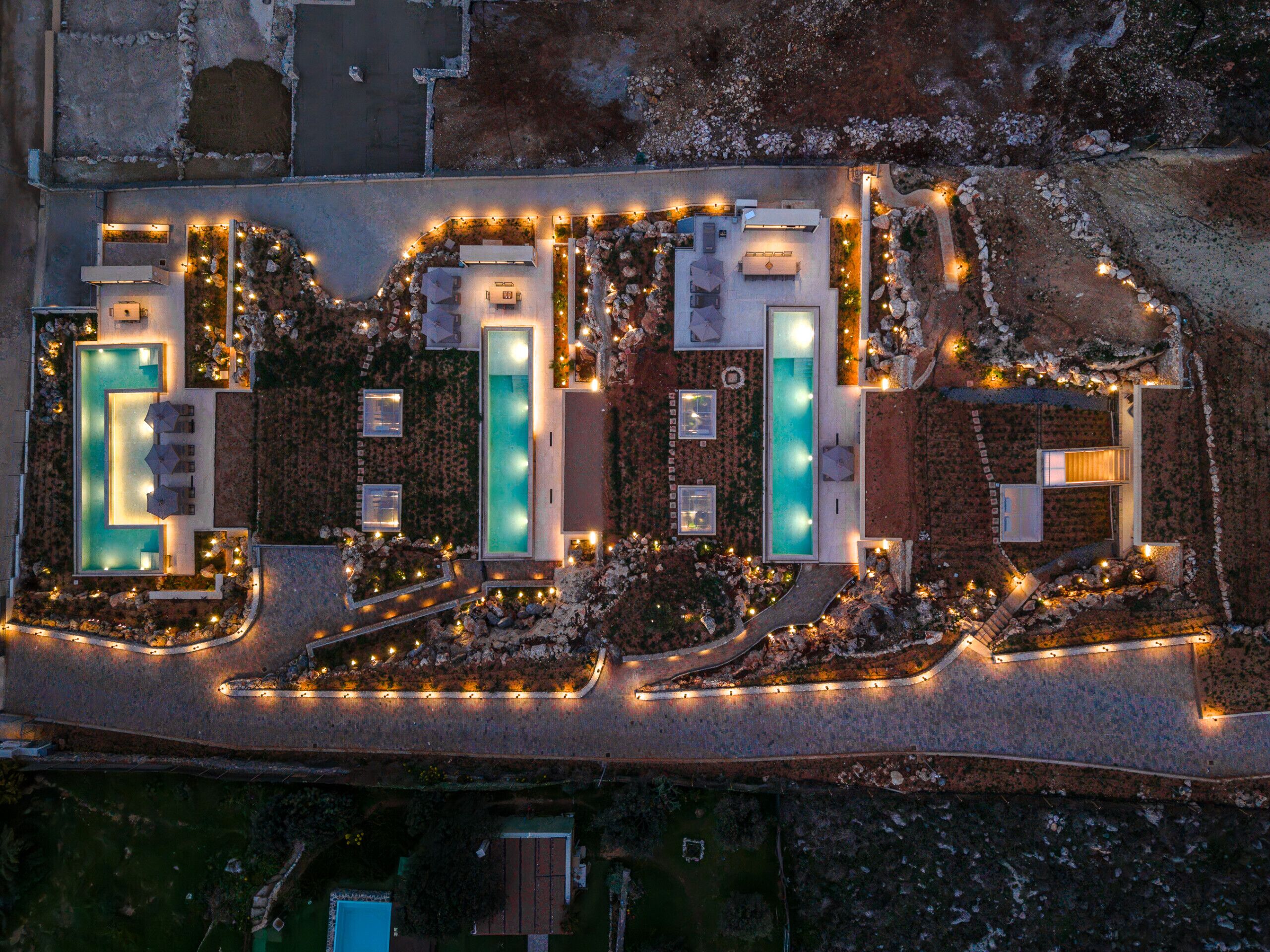 An aerial view of a resort with multiple swimming pools, outdoor seating areas, and well-lit pathways.