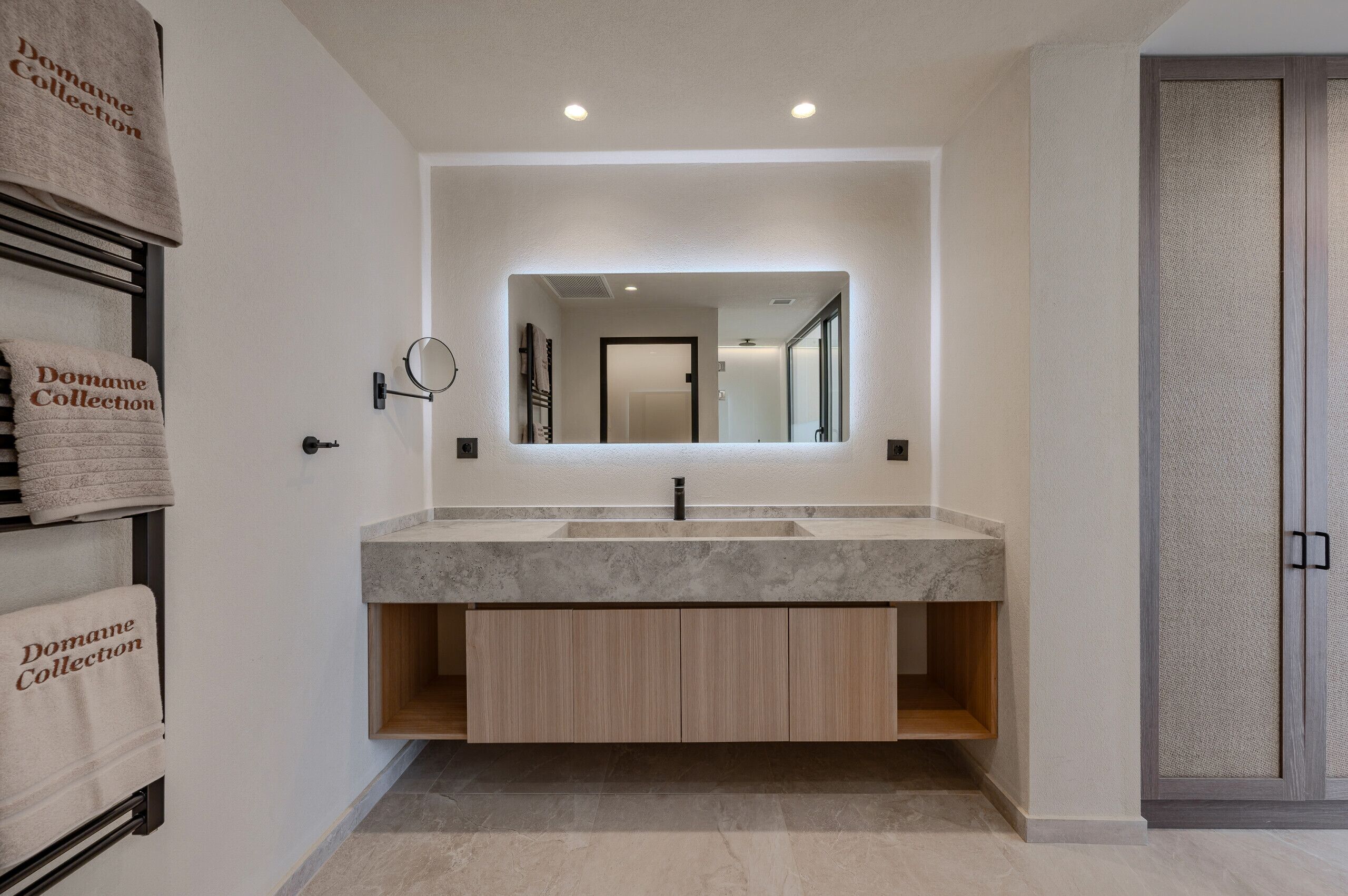 A modern bathroom with a marble sink, wooden cabinets, a large mirror, and a towel rack with 'Domaine Collection' towels.