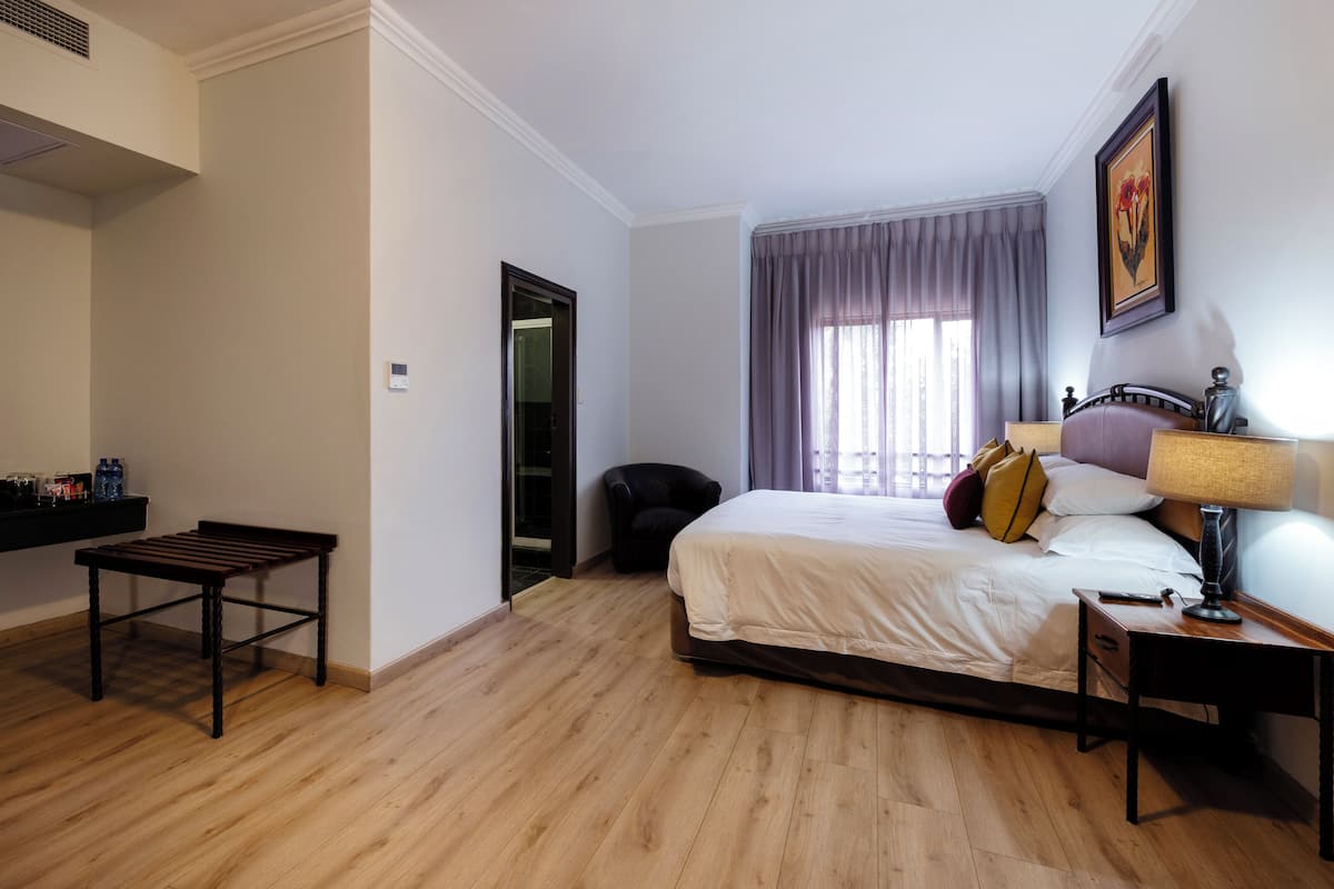 A bedroom with a bed, a bedside table, a chair, a wooden bench, and a window with curtains.