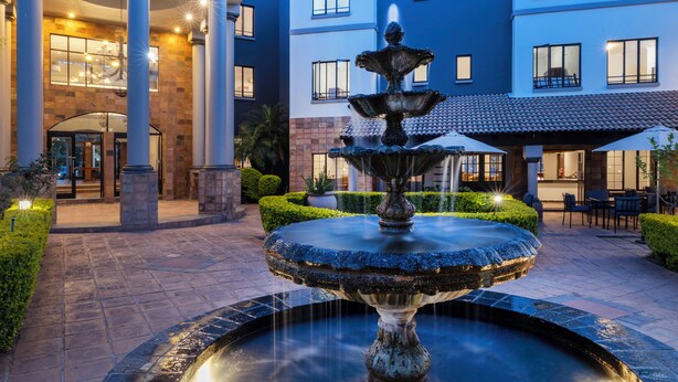 A courtyard with a central fountain, a building with multiple windows, and a well-maintained hedge.
