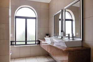 Un baño moderno con un amplio ventanal de arco, un lavabo doble y un espejo grande.