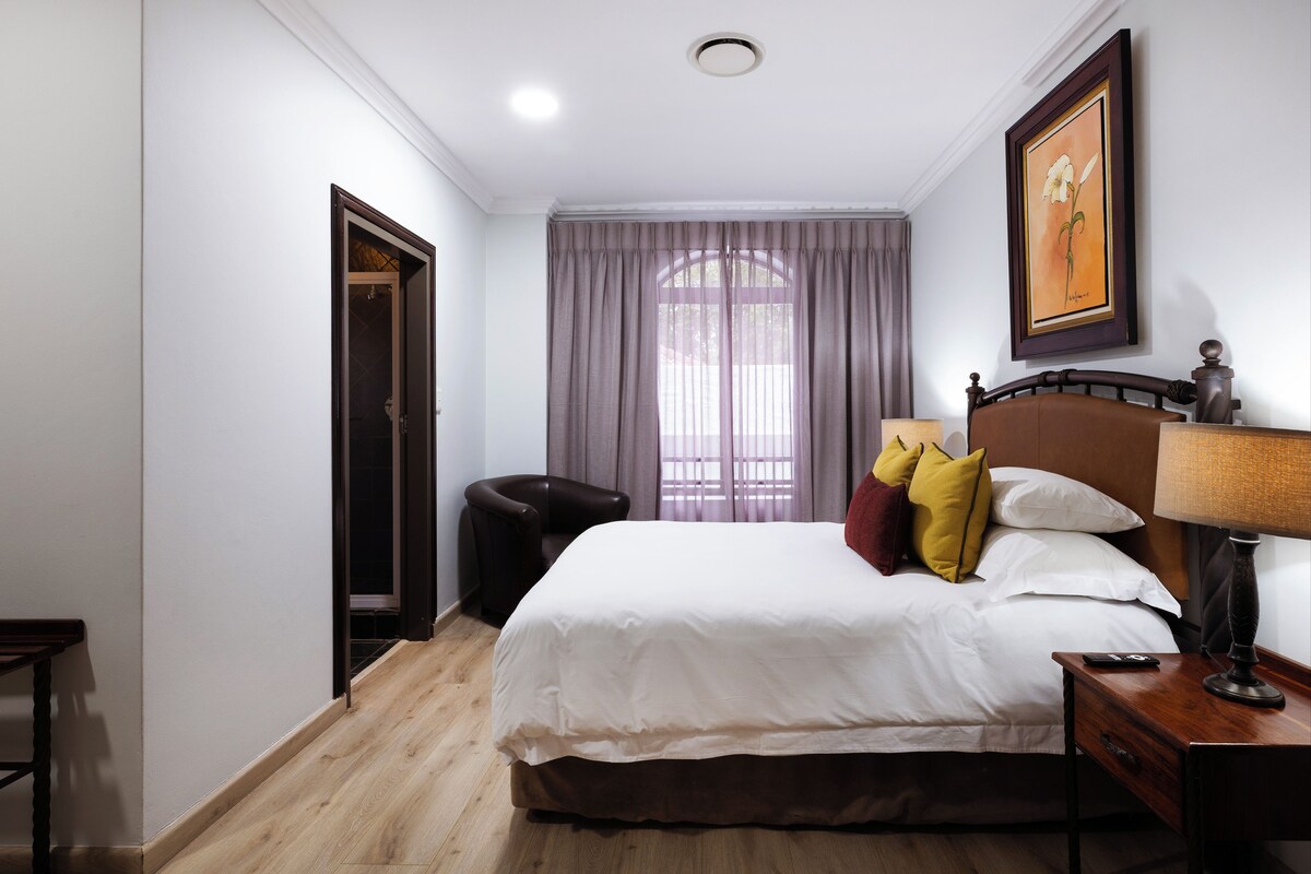 A hotel room with a bed, a chair, a desk, a lamp, and a framed picture on the wall.