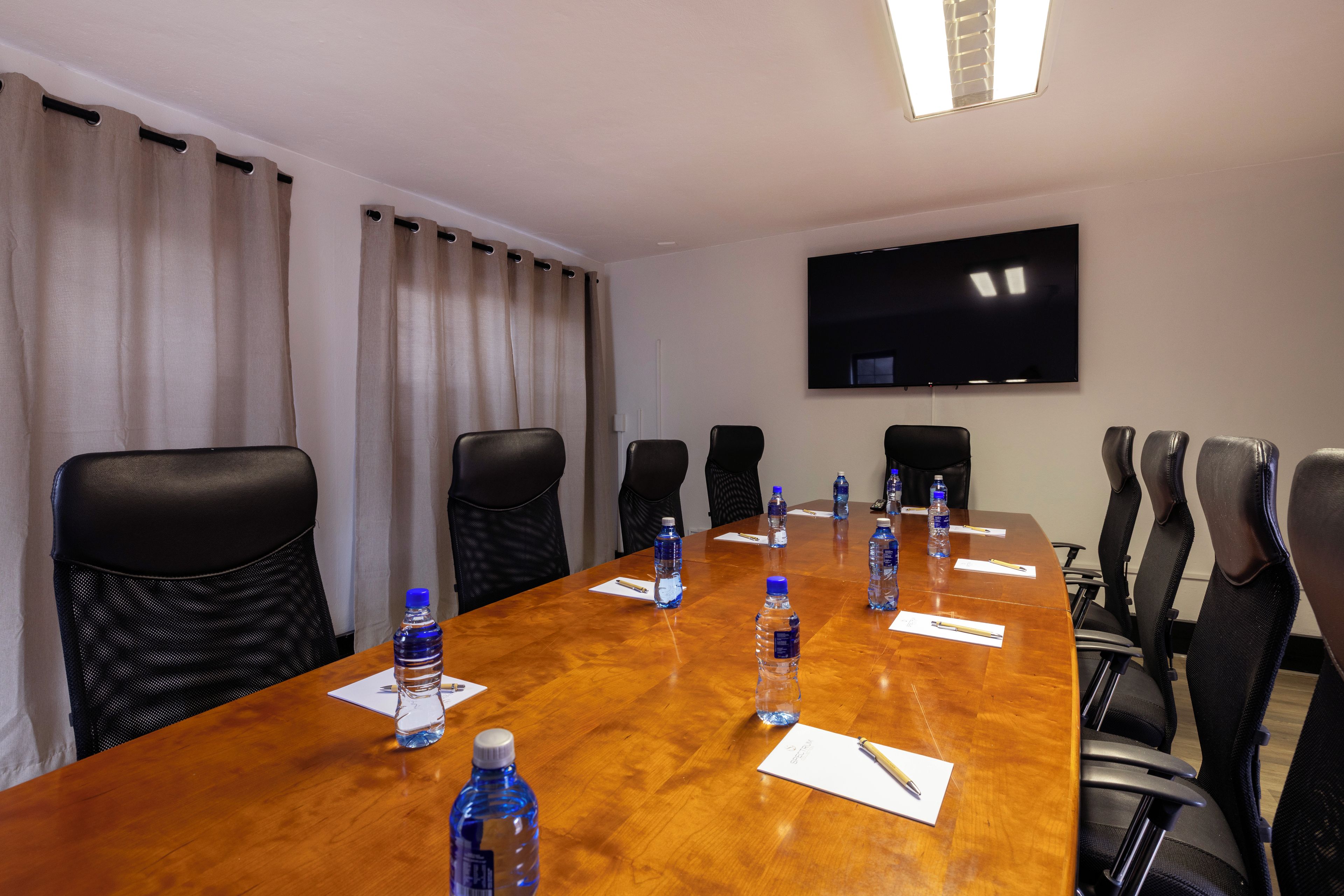 A conference room with a long table, chairs, water bottles, and a flat-screen TV on the wall.